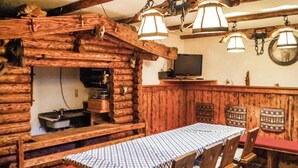 Un intérieur rustique en bois, avec une table à carreaux, des chaises en bois, un coin bar et un téléviseur fixé au mur.