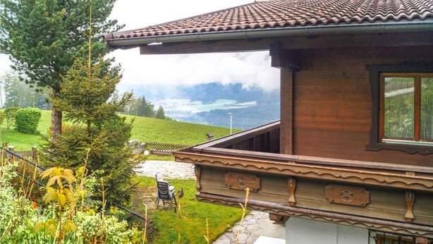 Une maison en bois avec un toit en tuiles, un chemin de pierre et une vue sur un paysage verdoyant et des montagnes.
