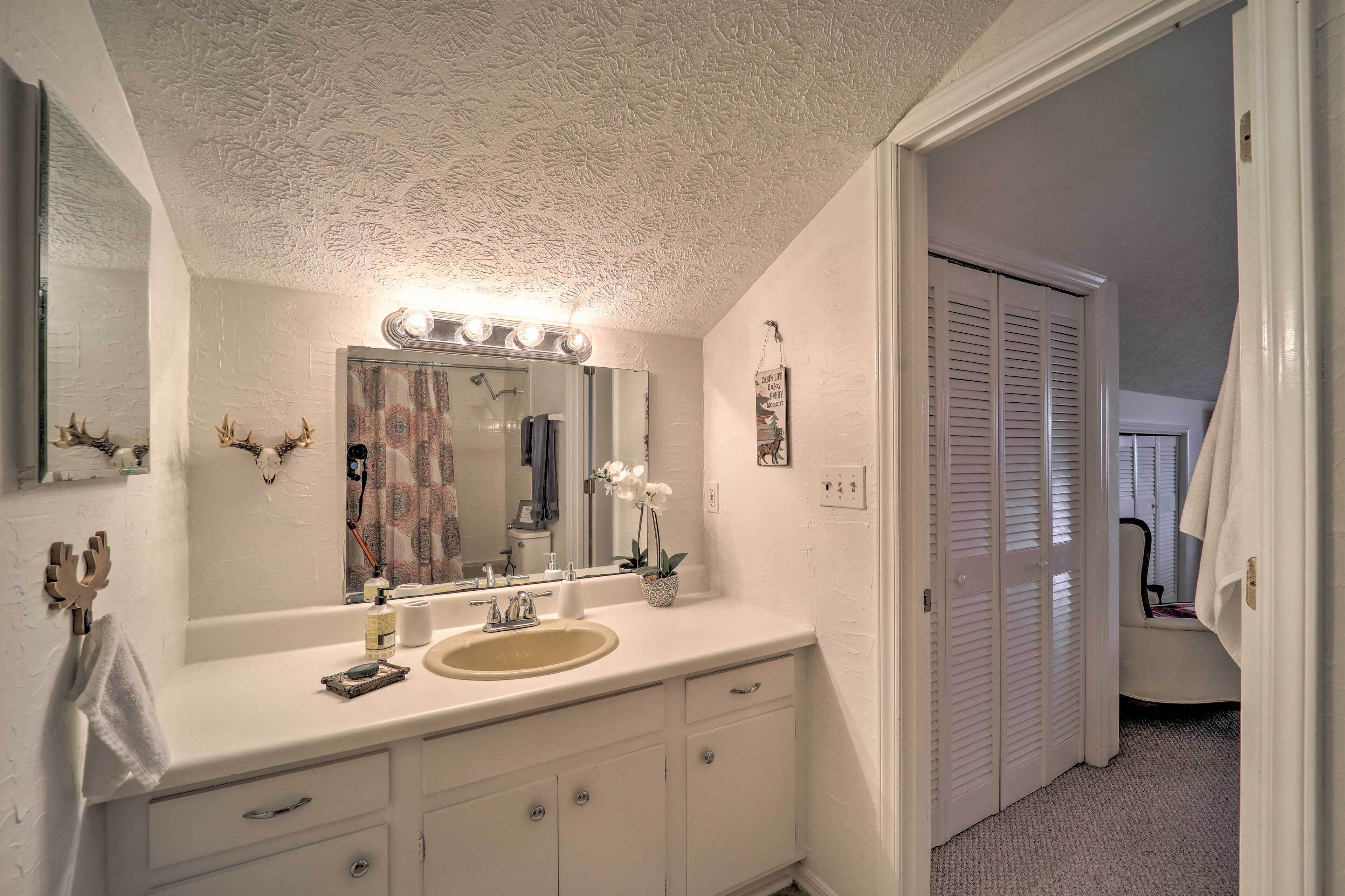 A bathroom with a white vanity, a mirror with lights, a sink, and a shower area.