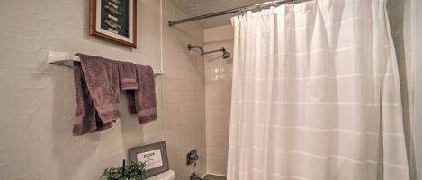 Ein Badezimmer mit Duschvorhang, einem gerahmten Bild an der Wand und einer Toilette mit einem Tablett für Pflegeprodukte.