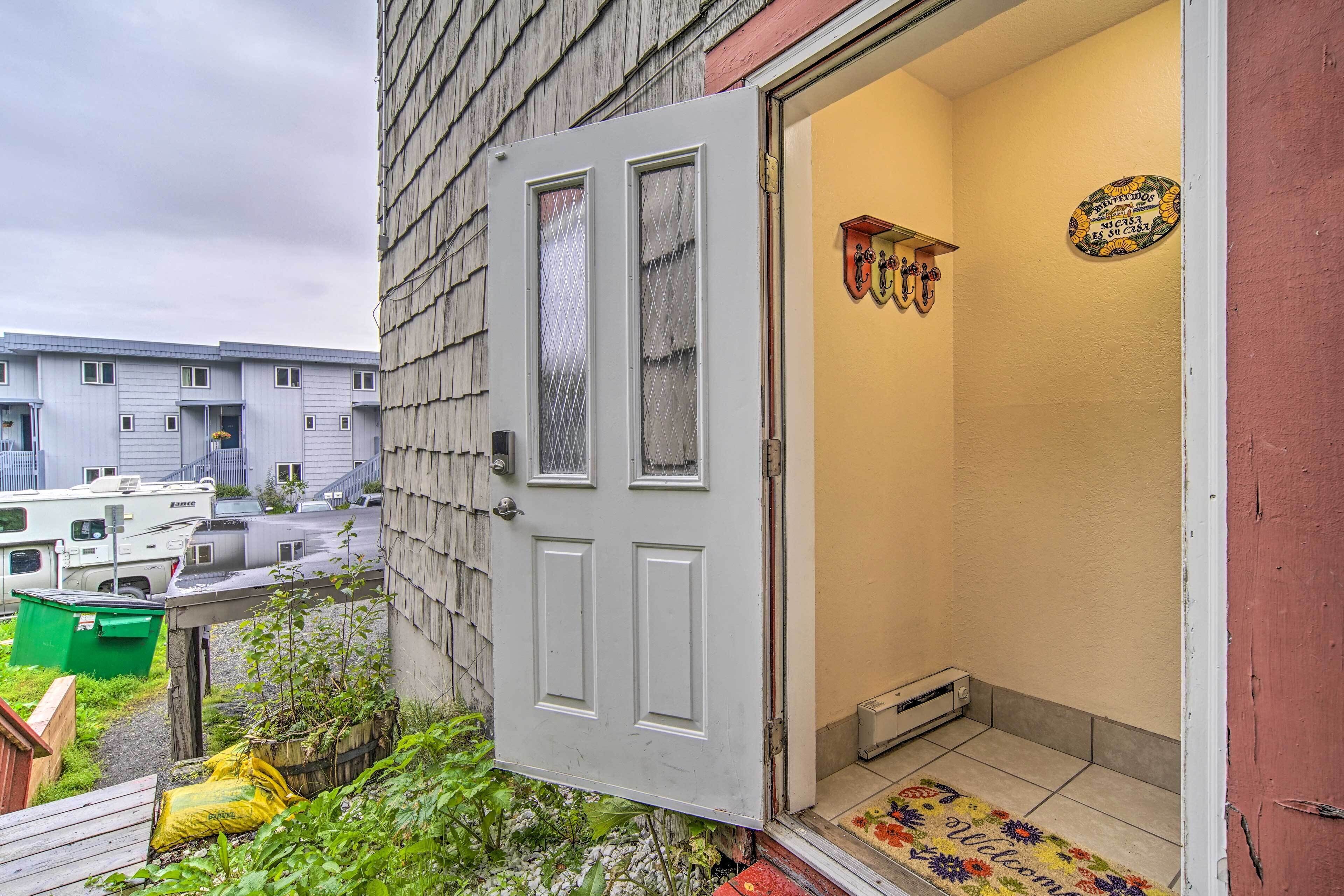 A residential building with a white door, a welcome mat, and a small garden area.