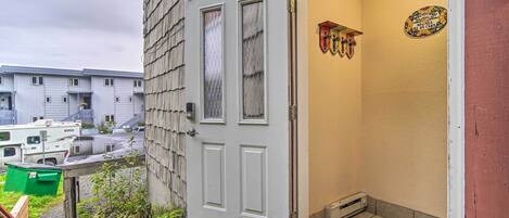 A residential building with a white door, a welcome mat, and a small garden area.
