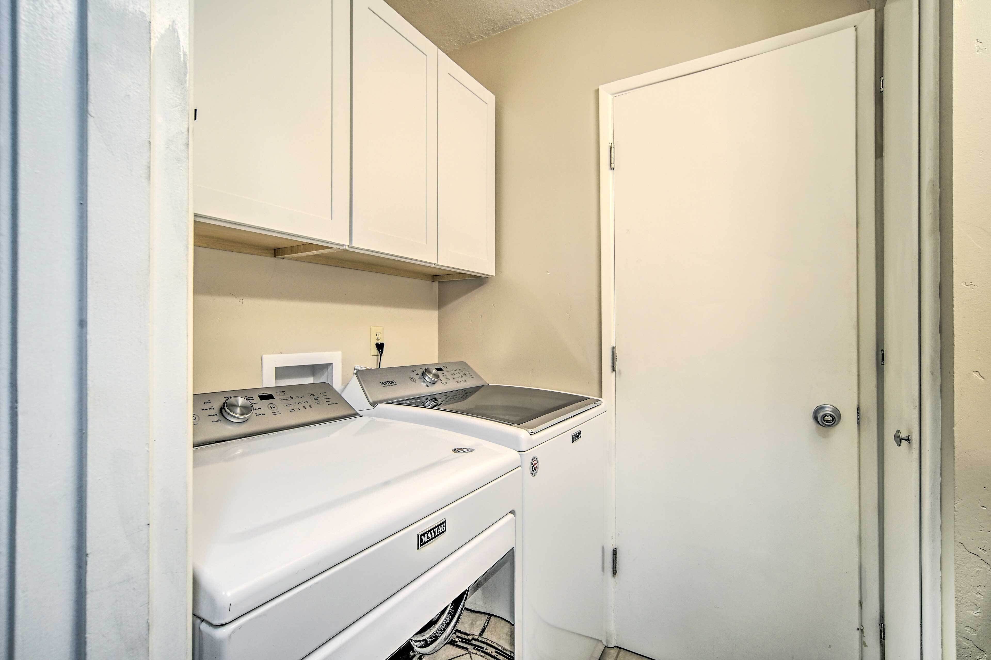 A laundry room with a front-loading washer and dryer, white cabinets above, and a closed door to the right.