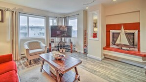 A living room with a TV, a sailboat model, a red sofa, and a wooden coffee table. - Walk to Downtown & Coast Trail: Condo in Anchorage (Anchorage)
