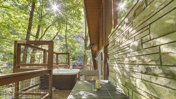 A wooden deck with a hot tub, a wicker chair, and a bottle of sunscreen. - Cabin w/ Hot Tub: 2 Mi to Downtown Gatlinburg! (Gatlinburg)