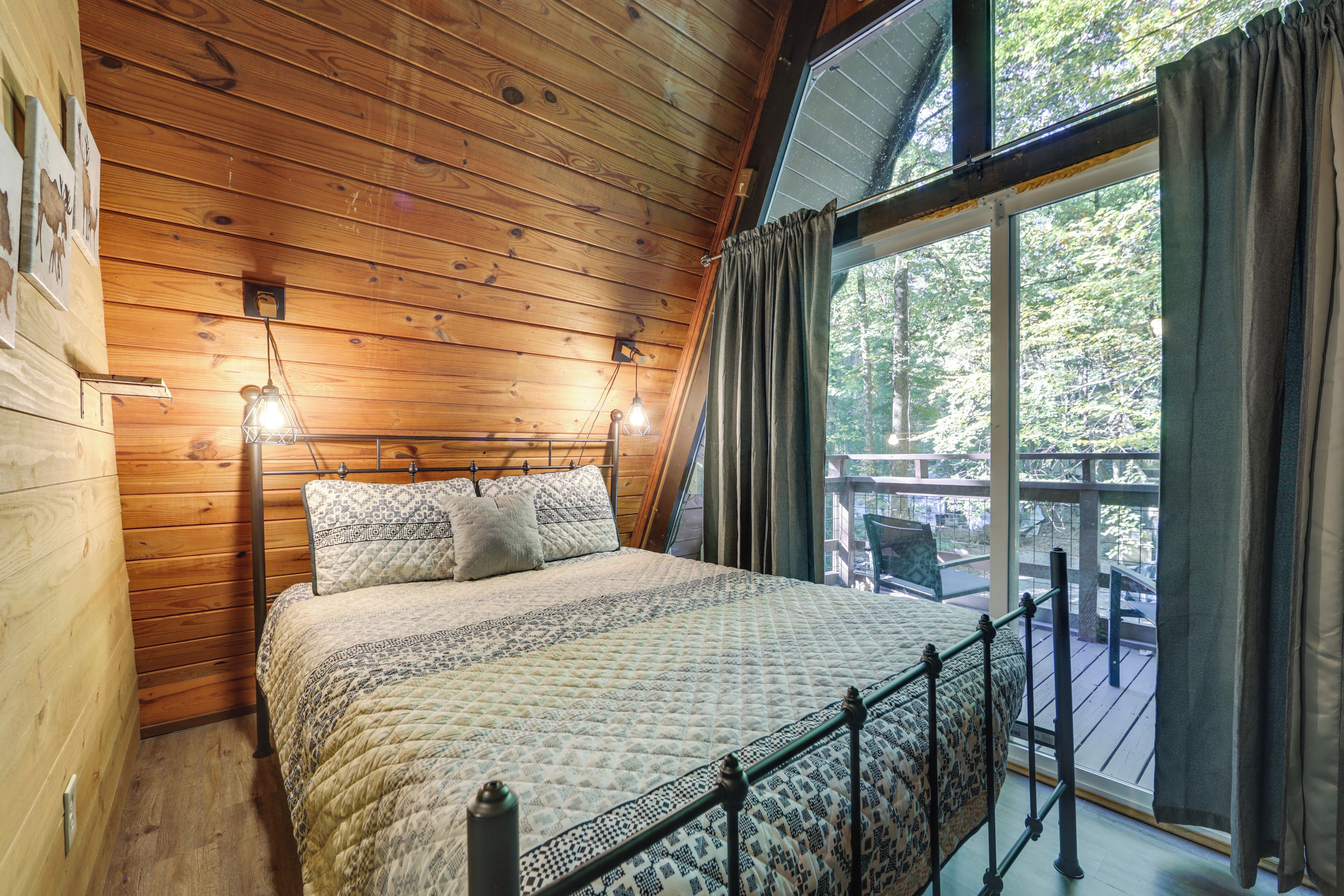 A wooden cabin bedroom with a bed, two wall-mounted lights, and a large window with curtains.