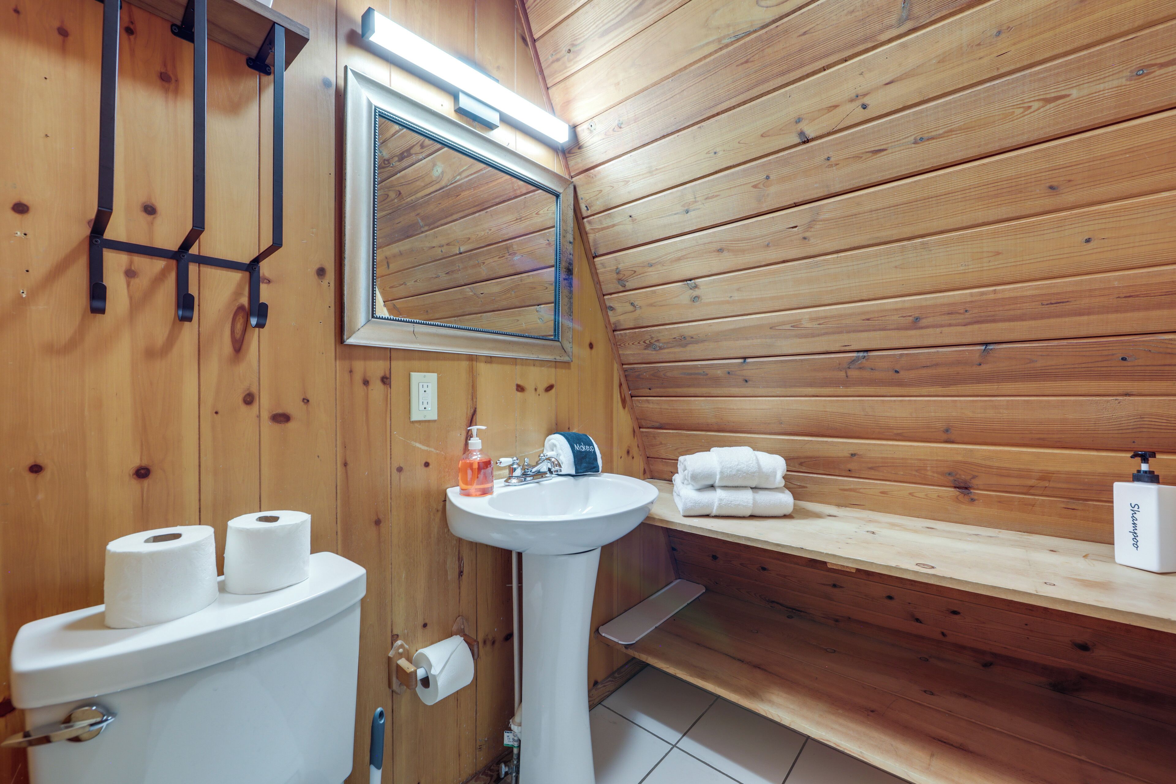 A wooden-paneled bathroom with a toilet, sink, mirror, and towel rack.