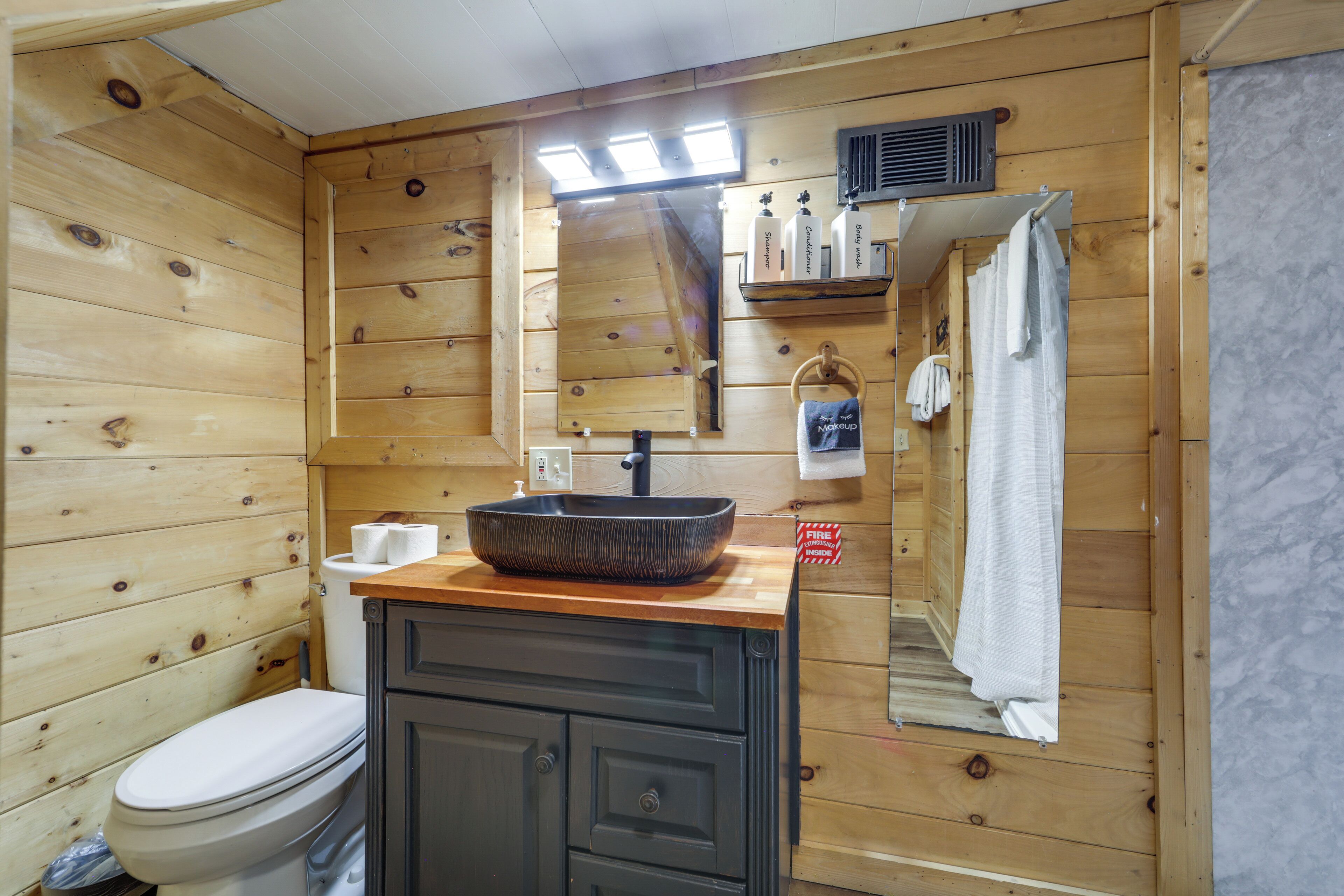 A wooden cabin-style bathroom with a toilet, sink, and mirror.