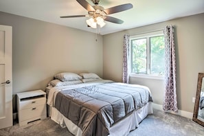 A bedroom with a bed, a nightstand, a ceiling fan, a window with curtains, and a door. - Cabin w/ Dock & Porch Across From Balsam Lake (Balsam Lake)
