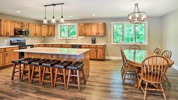 Una cocina moderna con armarios de madera, una isla grande con taburetes de bar, una mesa de comedor con sillas e iluminación colgante.
