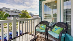 A balcony with wicker chairs and a glass table, overlooking a street with parked cars and buildings. - Breezy Wildwood Condo ~ 2 Blocks to Beach! (Wildwood)