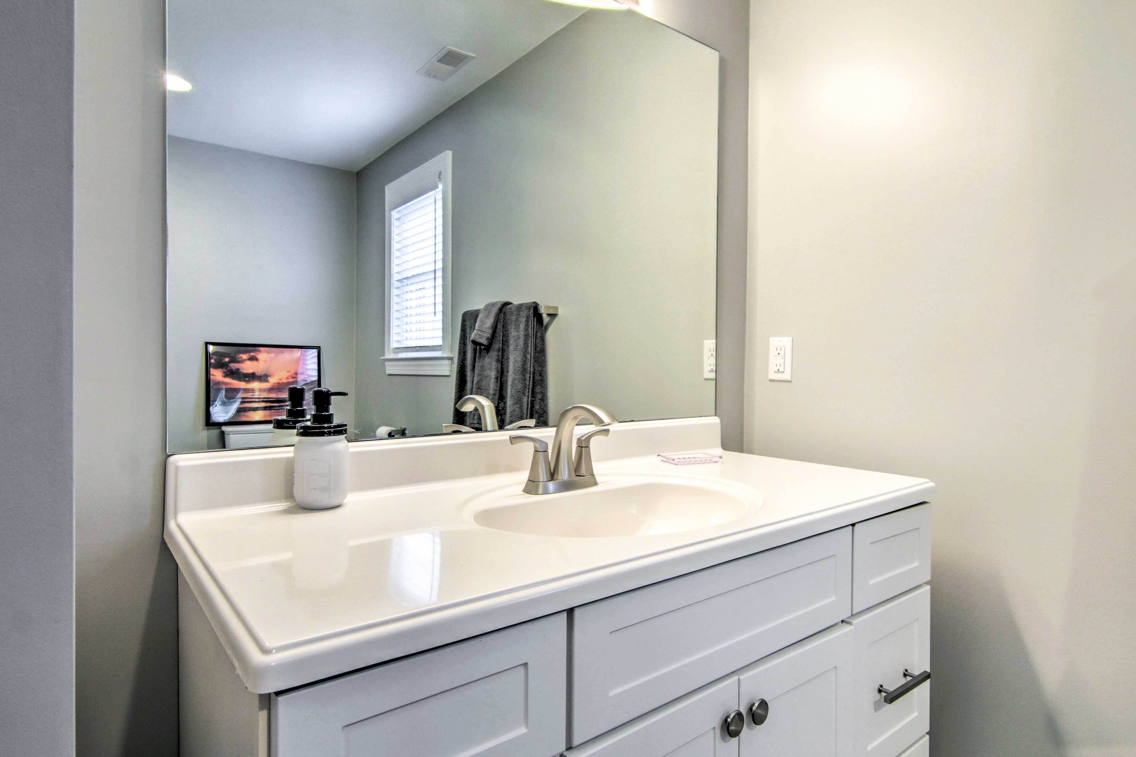 Une salle de bain avec un meuble-lavabo blanc, un grand miroir et une fenêtre avec des stores.
