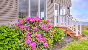 Ein Haus mit großen Fenstern, einer Holzterrasse und einem Garten mit rosa Blumen.