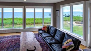 Ein geräumiges Wohnzimmer mit einem großen Fenster mit Blick auf das Meer und eine grüne Landschaft.