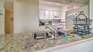 Una cocina con encimera de granito, pileta de acero inoxidable y escurreplatos.