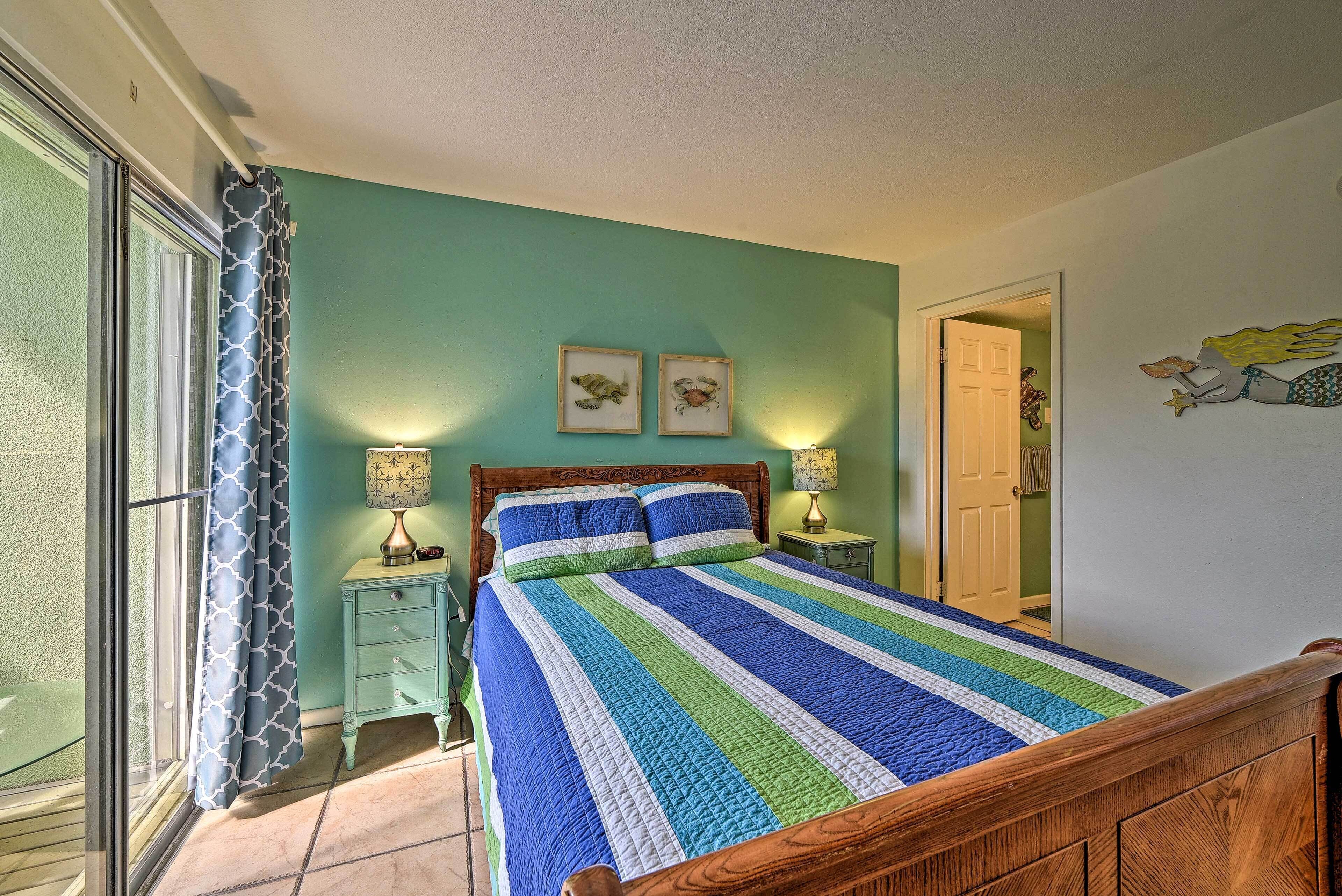 A bedroom with a bed, a nightstand, a lamp, a door, and a wall with two framed pictures.