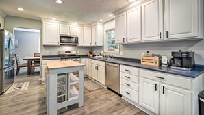 A modern kitchen with white cabinets, stainless steel appliances, and a wooden dining table. - Beulah Family Home ~ 2 Mi to Dtwn + Beach! (Beulah)