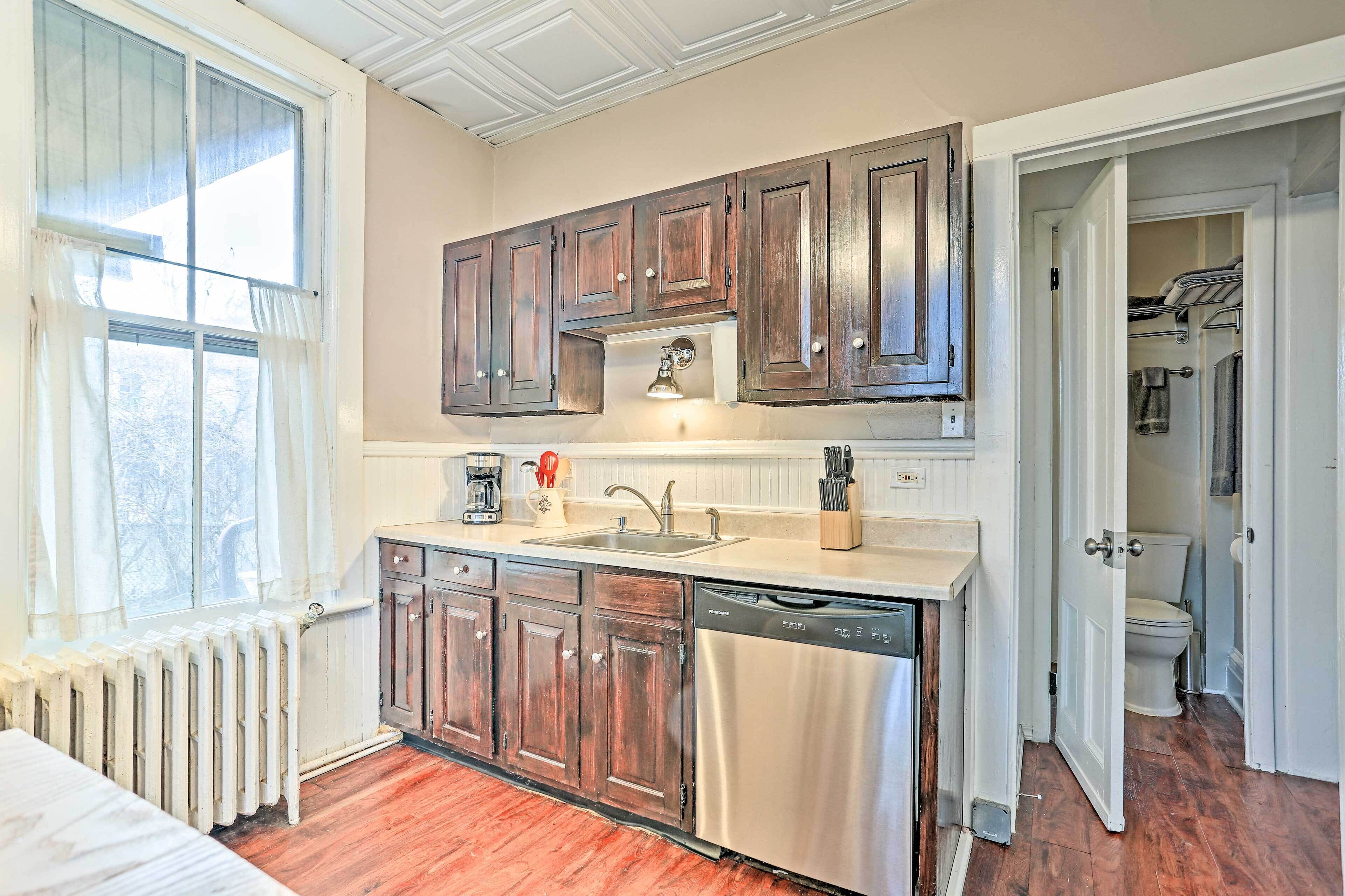 A compact kitchen with wooden cabinets, a dishwasher, and a window with curtains.
