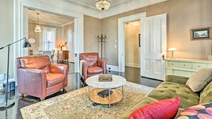 A living room with a brown leather armchair, a green sofa, a round coffee table, and a chandelier. - Centrally Located Apt in Victorian Mansion! (Poughkeepsie)