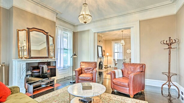 A spacious living room with leather armchairs, a round coffee table, a fireplace, and a chandelier. - Centrally Located Apt in Victorian Mansion! (Poughkeepsie)