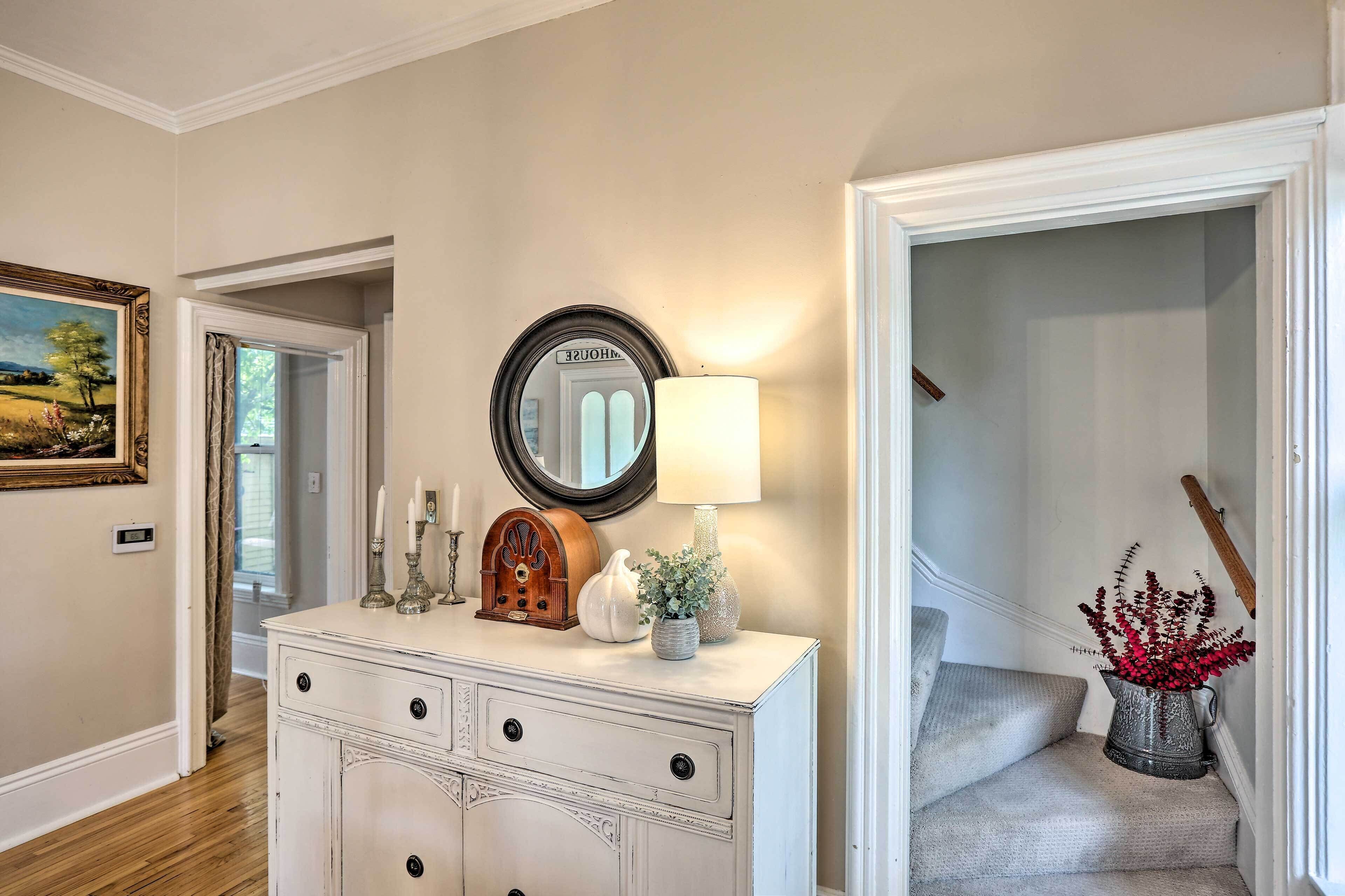 A hallway with a white dresser, a mirror, a lamp, a vintage radio, and a painting on the wall.