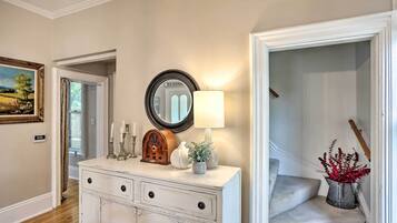A hallway with a white dresser, a mirror, a lamp, a vintage radio, and a painting on the wall.