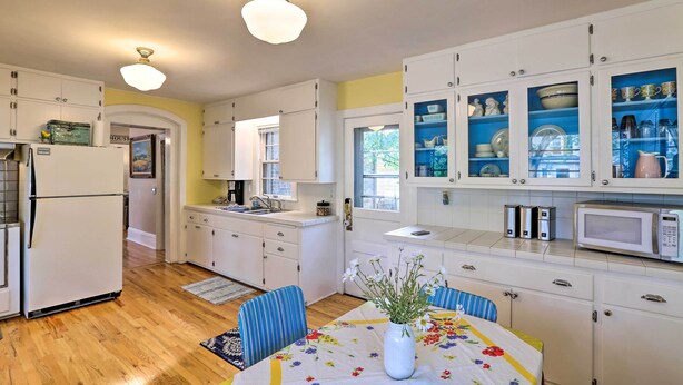 Una cocina con armarios blancos, un refrigerador, un microondas y una mesa de comedor con sillas.