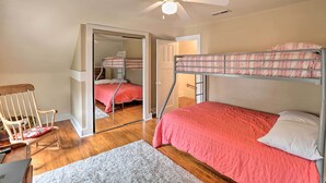 Un dormitorio con una cama litera, una mecedora de madera, una alfombra blanca y un ventilador de techo.