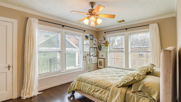 Une chambre à coucher avec un lit, un ventilateur de plafond et de grandes fenêtres équipées de stores.