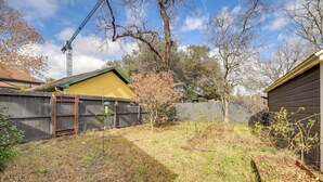 Un jardin avec une clôture en bois, un arbre et un bâtiment jaune.