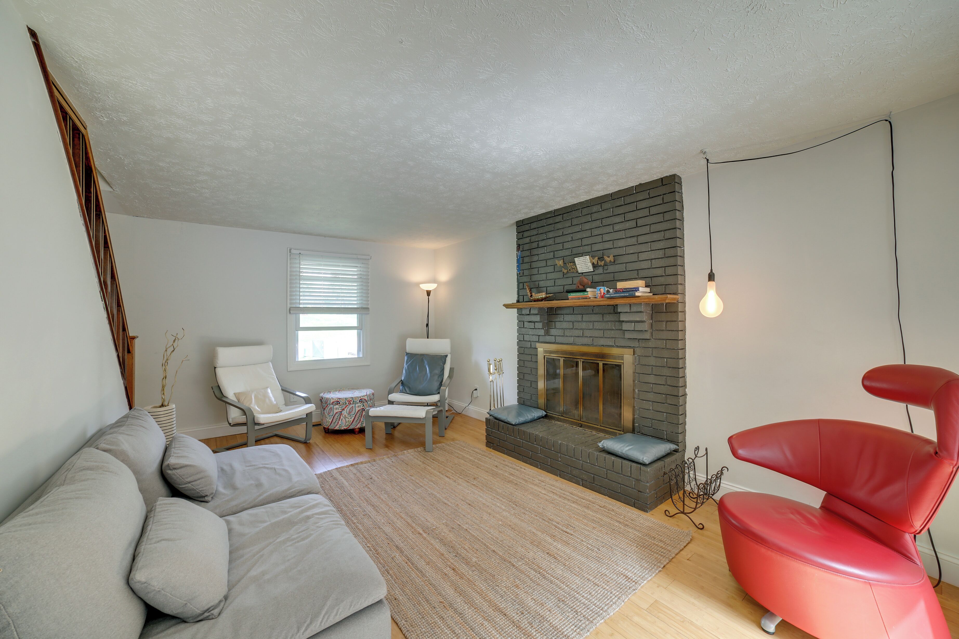 A living room with a fireplace, a red chair, a grey sofa, and a white armchair.