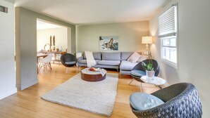 Una sala de estar con un sofá gris, dos sillones, una mesa de centro y una zona de comedor con una mesa y sillas.
