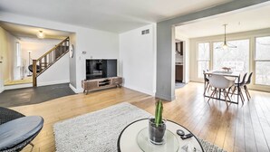Amplia sala de estar con escalera, una mesa de comedor con sillas, un televisor y una planta de cactus.
