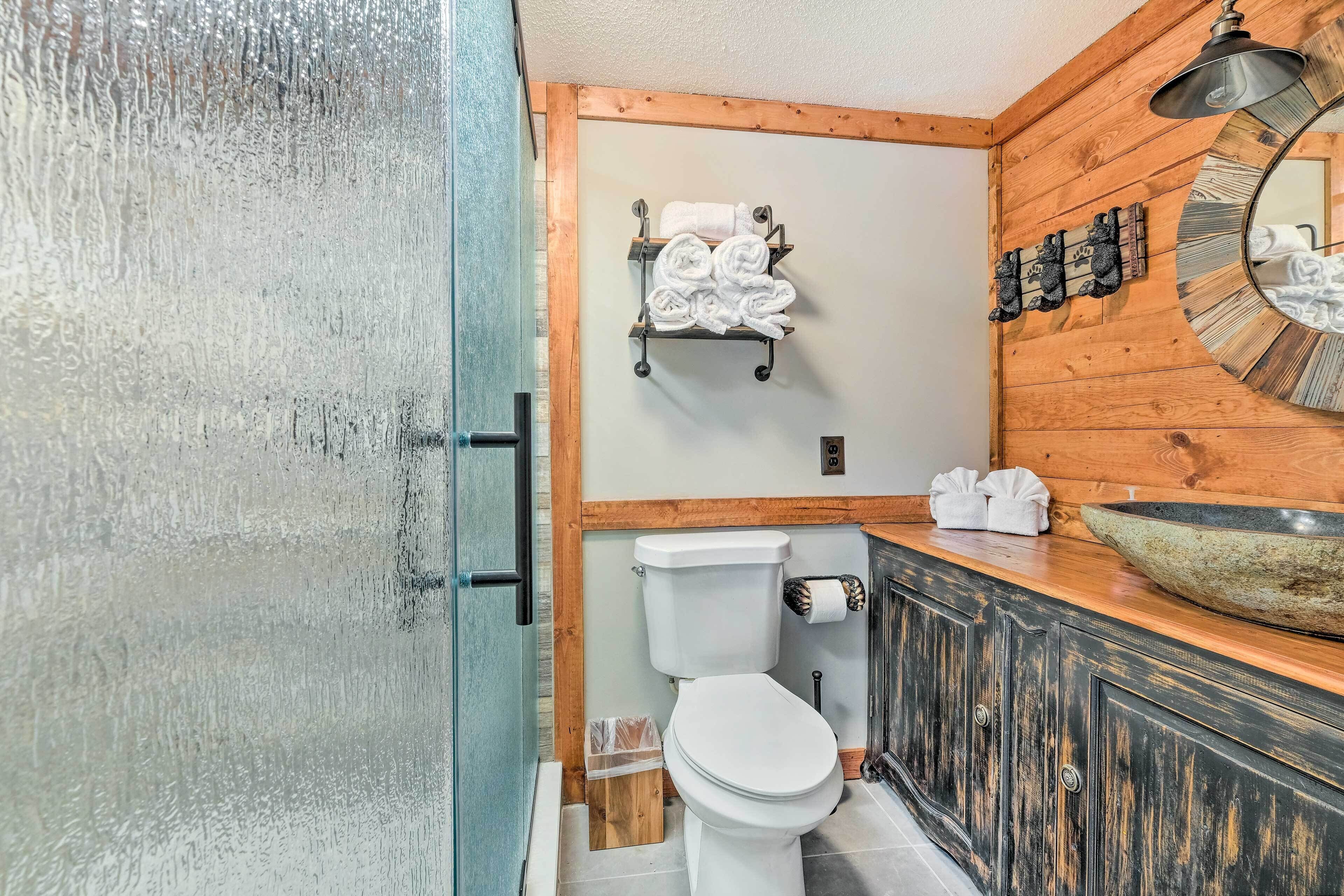 A bathroom with a wooden wall, a white toilet, a sink with a large basin, and a towel rack with towels.