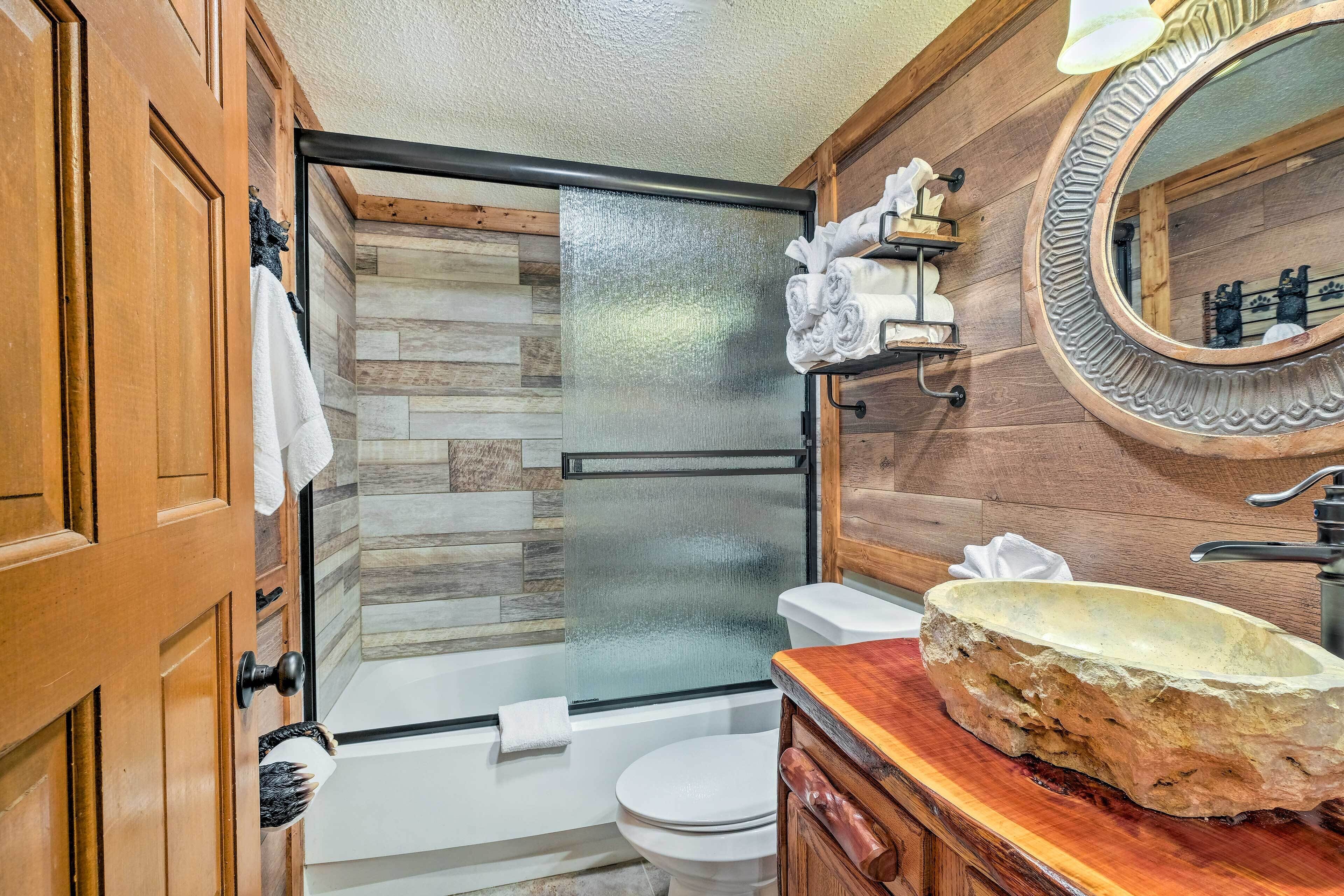 Un baño con ducha de vidrio, tocador de madera con lavamanos de piedra y un espejo con marco decorativo.