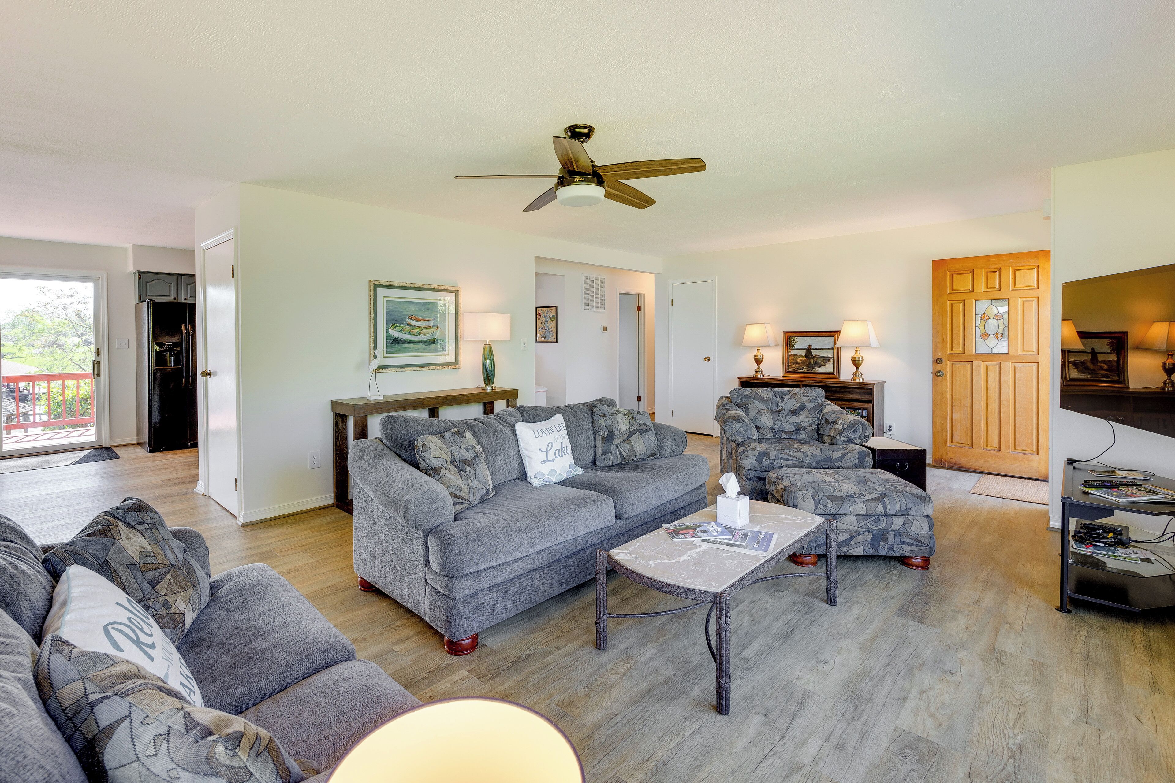 A spacious living room with a grey sofa, patterned armchairs, a coffee table, and a ceiling fan.