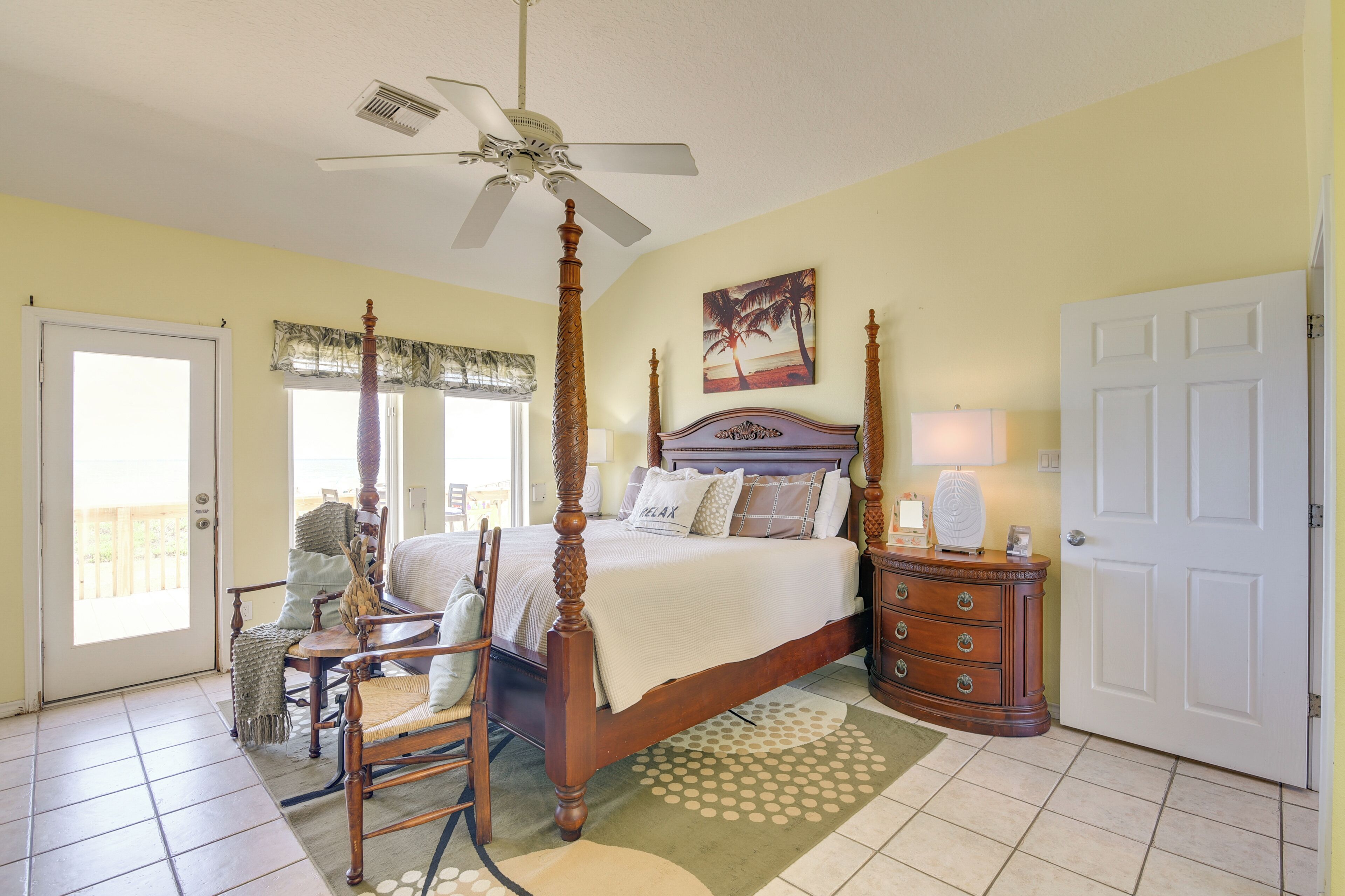 A bedroom with a four-poster bed, a ceiling fan, a wooden dresser, and a door leading to a balcony.