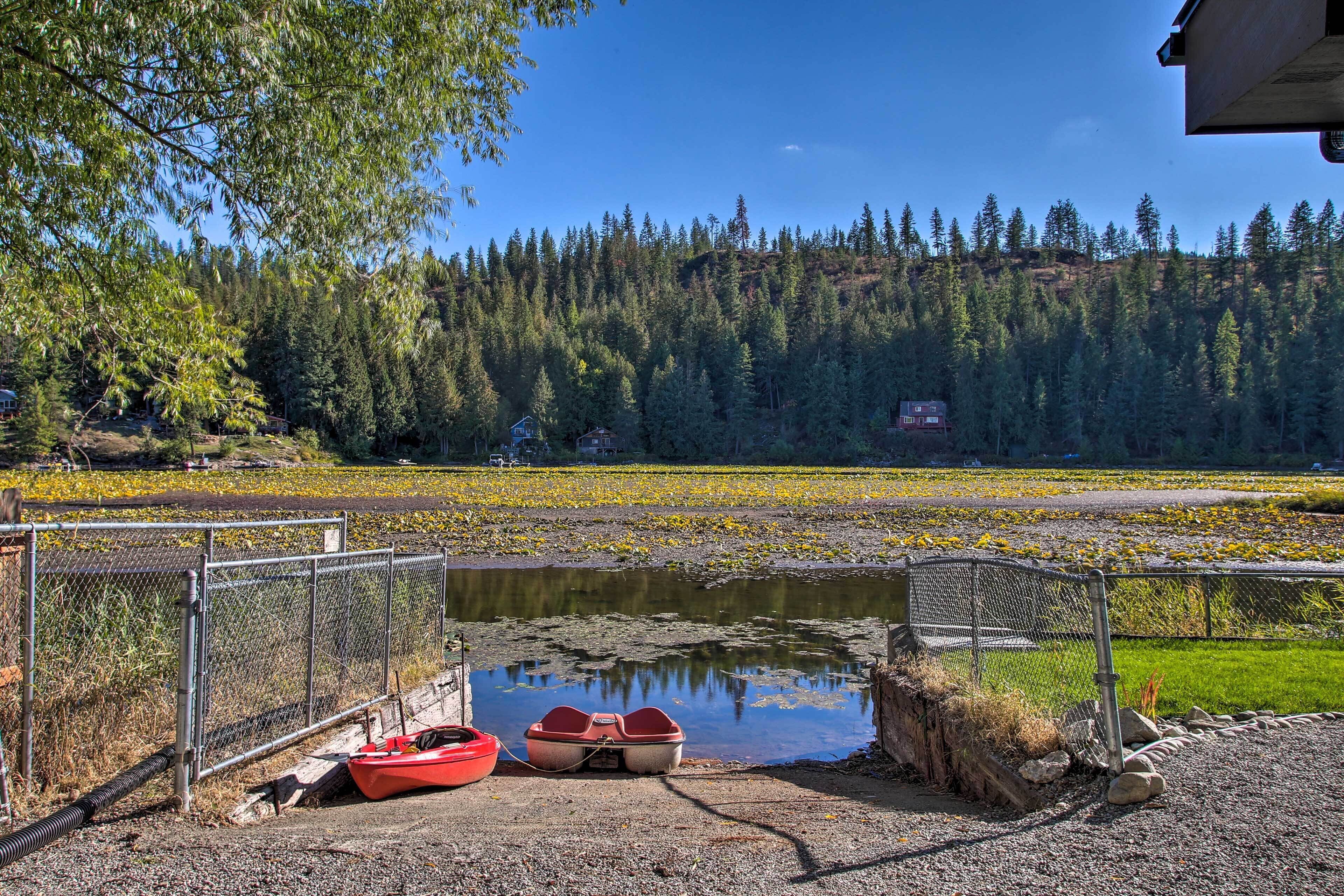 Un paisaje tranquilo junto al lago con un muelle de madera, un bote pequeño y una colina boscosa al fondo.