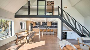 A spacious kitchen with a high ceiling, a dining area with a wooden table and chairs, and a staircase leading to an upper level. - A Contemporary Dream: Lakefront Rathdrum Oasis! (Rathdrum)