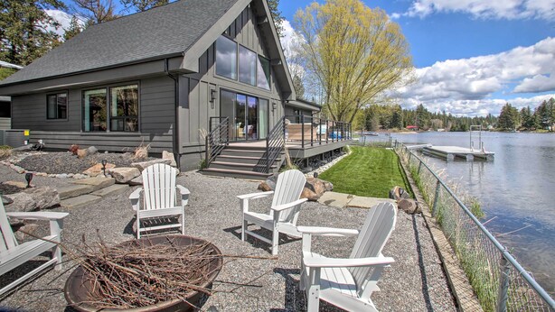 A modern house with a deck overlooking a lake, featuring Adirondack chairs and a fire pit. - A Contemporary Dream: Lakefront Rathdrum Oasis! (Rathdrum)