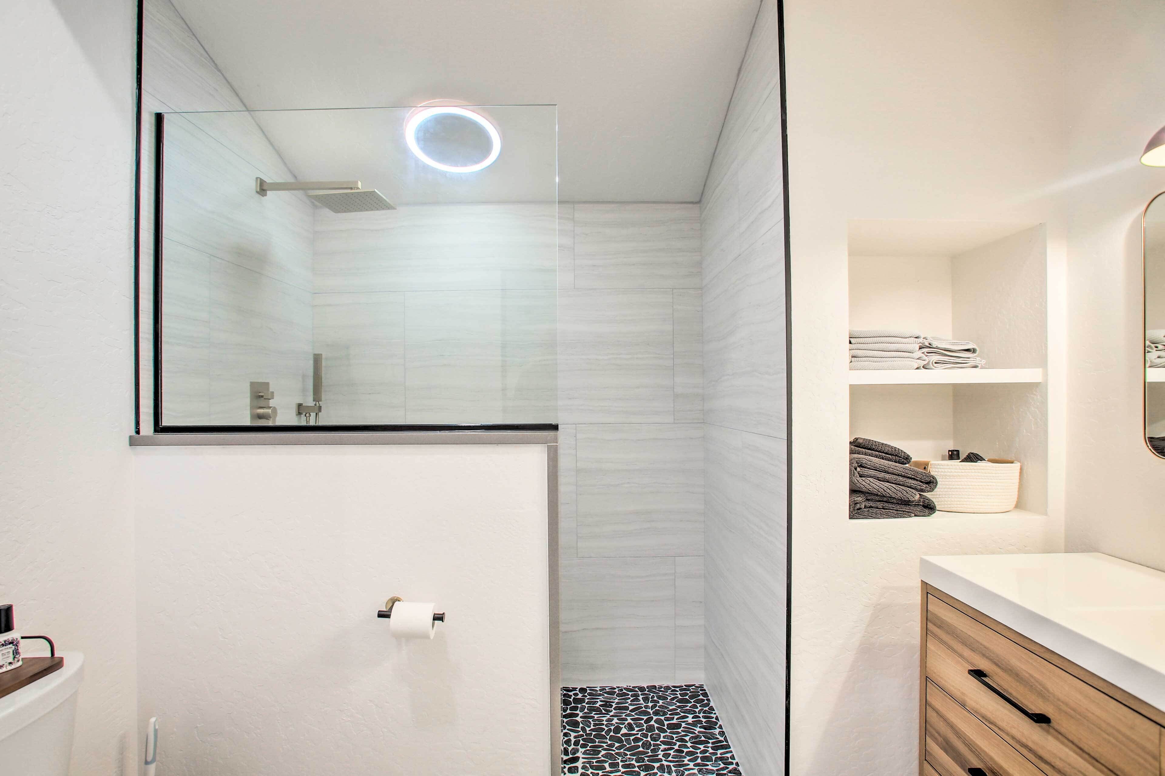 A modern bathroom with a glass shower enclosure, a toilet, a sink with a mirror, and a towel rack.