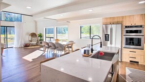 A modern kitchen with a large island, built-in appliances, and a dining area with natural light. - A Contemporary Dream: Lakefront Rathdrum Oasis! (Rathdrum)