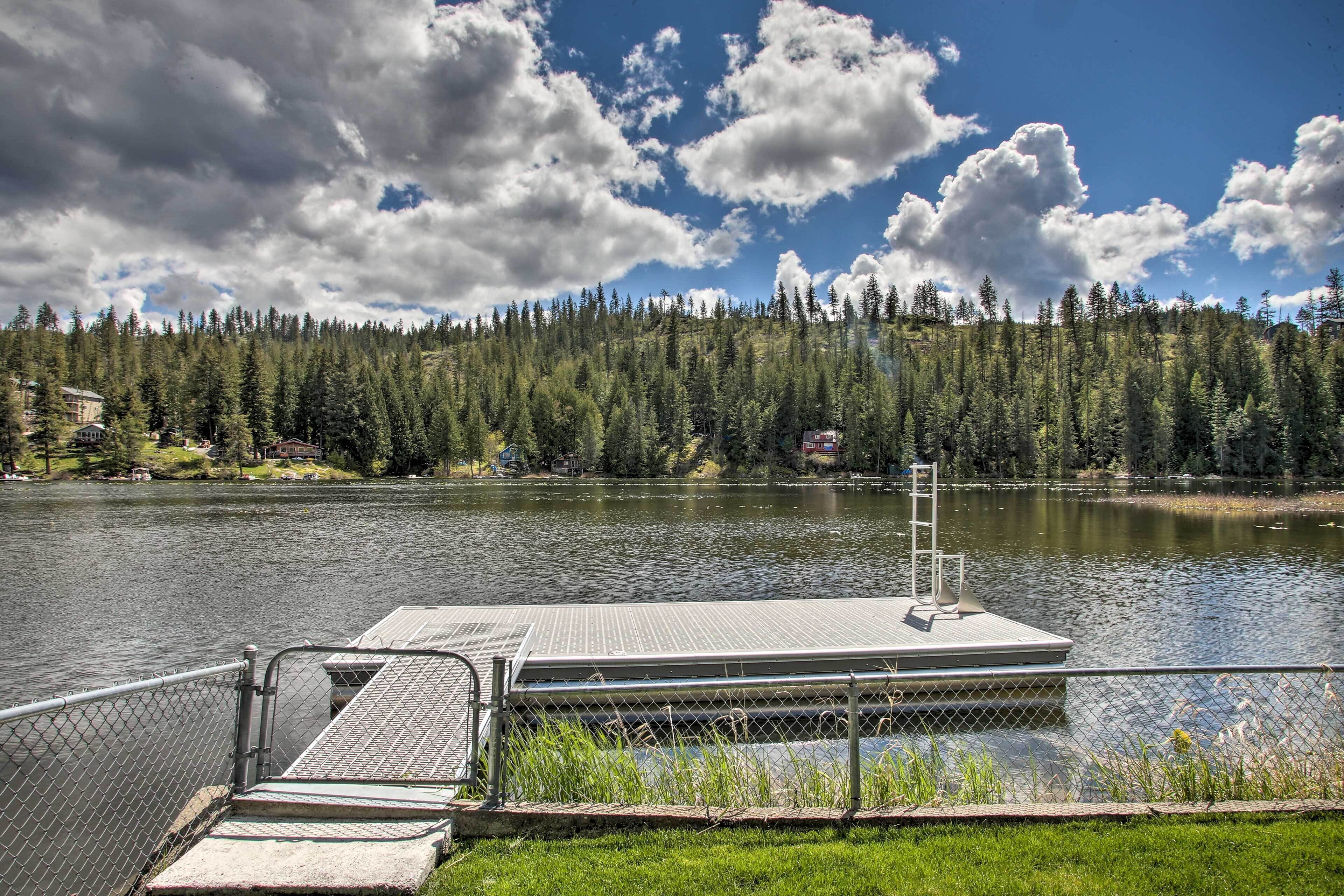 A dock extending into a lake with a forested hillside in the background.