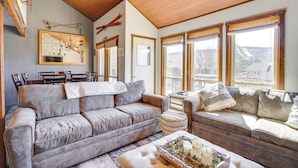 A cozy living room with a grey sofa, a wooden ceiling, and large windows offering a view of the outside. - Charming Townhome - Walk to Greek Peak Mountain! (Cortland)