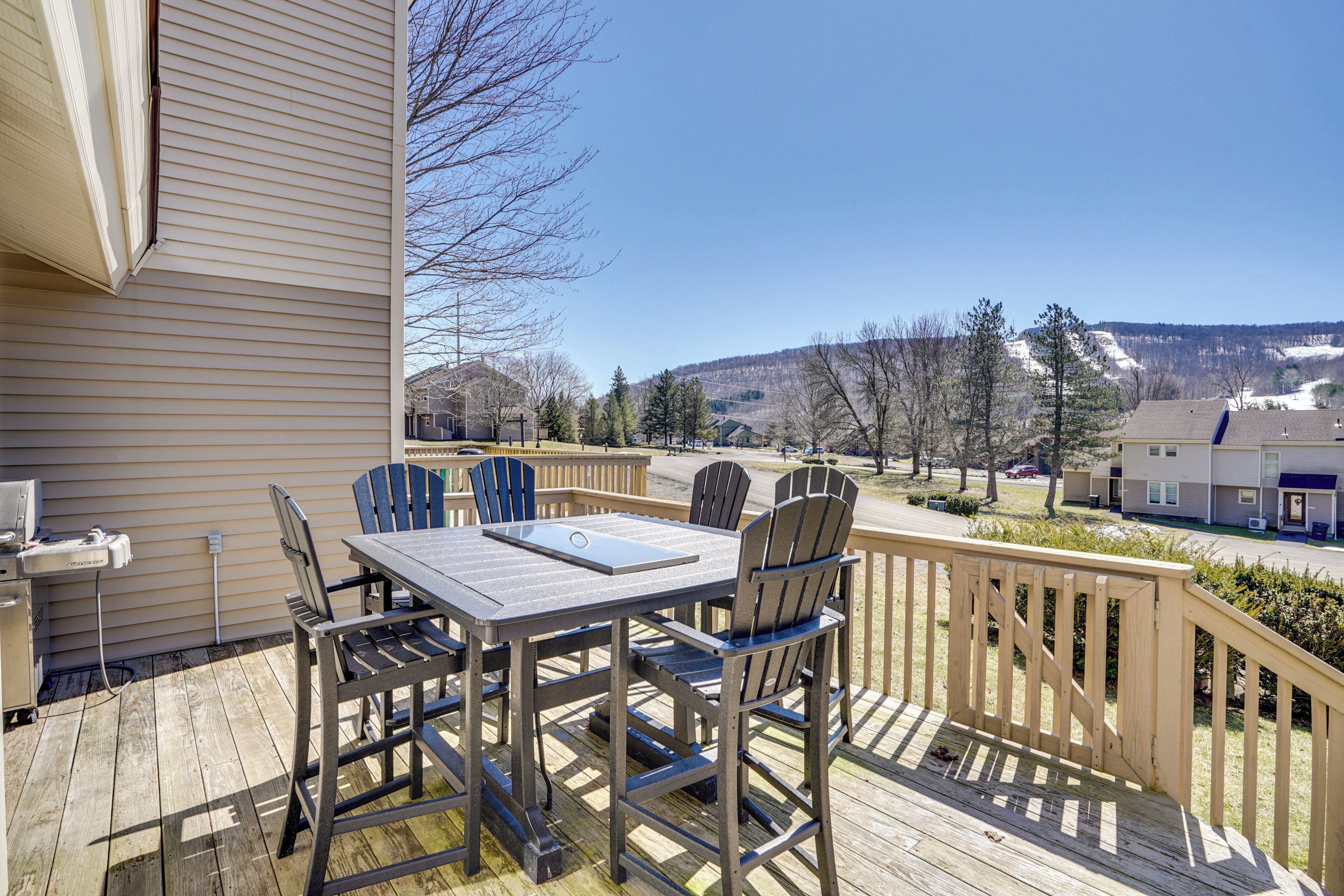 A wooden deck with a table and chairs, overlooking a residential area with houses and a mountain in the background.