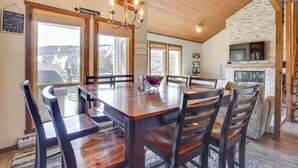 A dining area with a wooden table and chairs, a chandelier, and a stone fireplace. - Charming Townhome - Walk to Greek Peak Mountain! (Cortland)