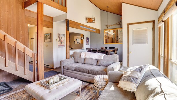 A spacious living room with a high ceiling, a grey sofa, a coffee table, and a staircase leading to an upper level. - Charming Townhome - Walk to Greek Peak Mountain! (Cortland)