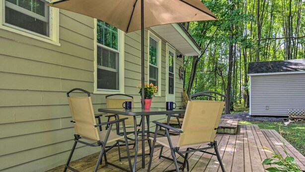 A wooden deck with a table and chairs, a potted plant, and a small shed in a wooded area. - Peaceful Finger Lakes Apartment With Patio! (Ovid)