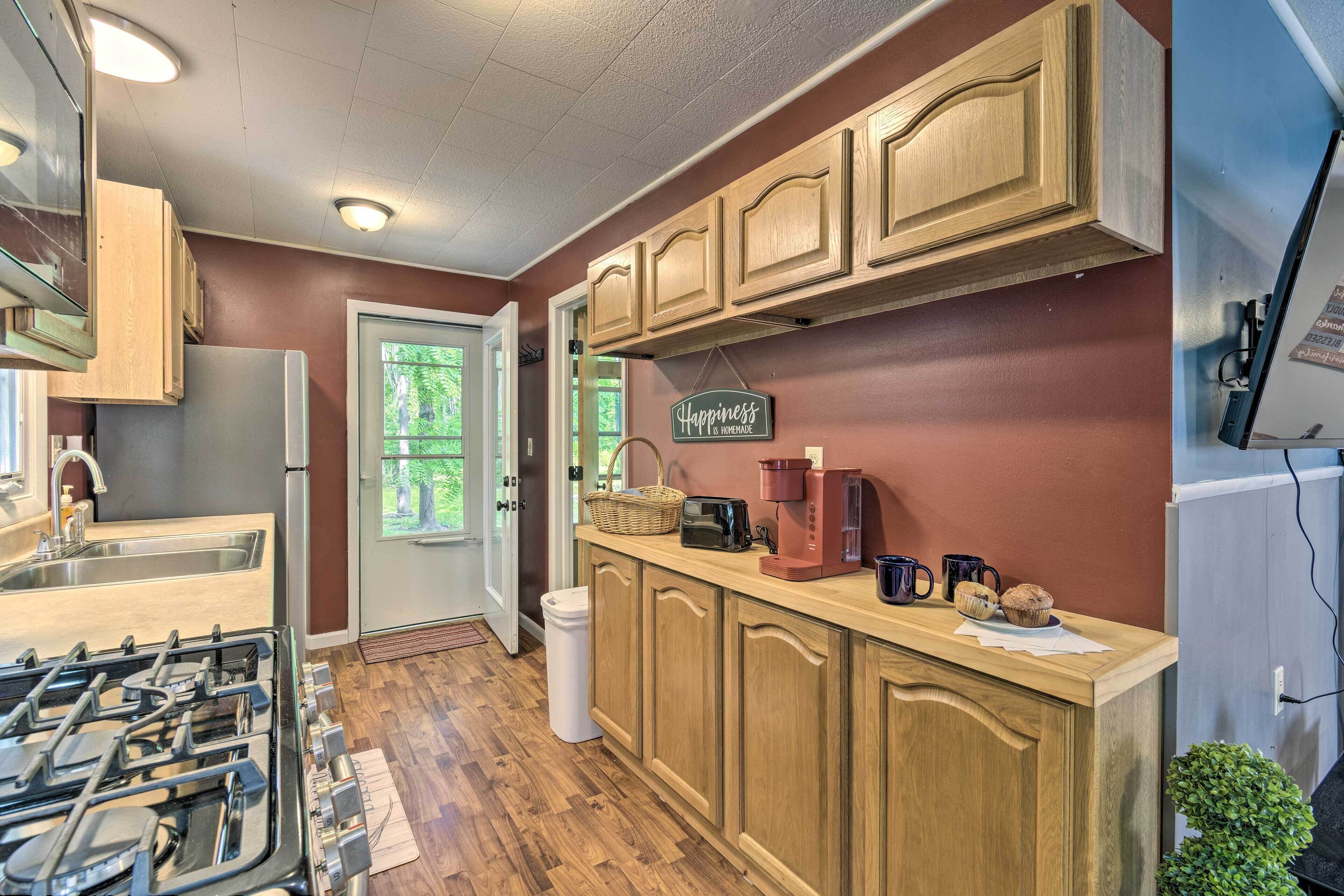 A kitchen with wooden cabinets, a gas stove, a coffee maker, and a trash can.