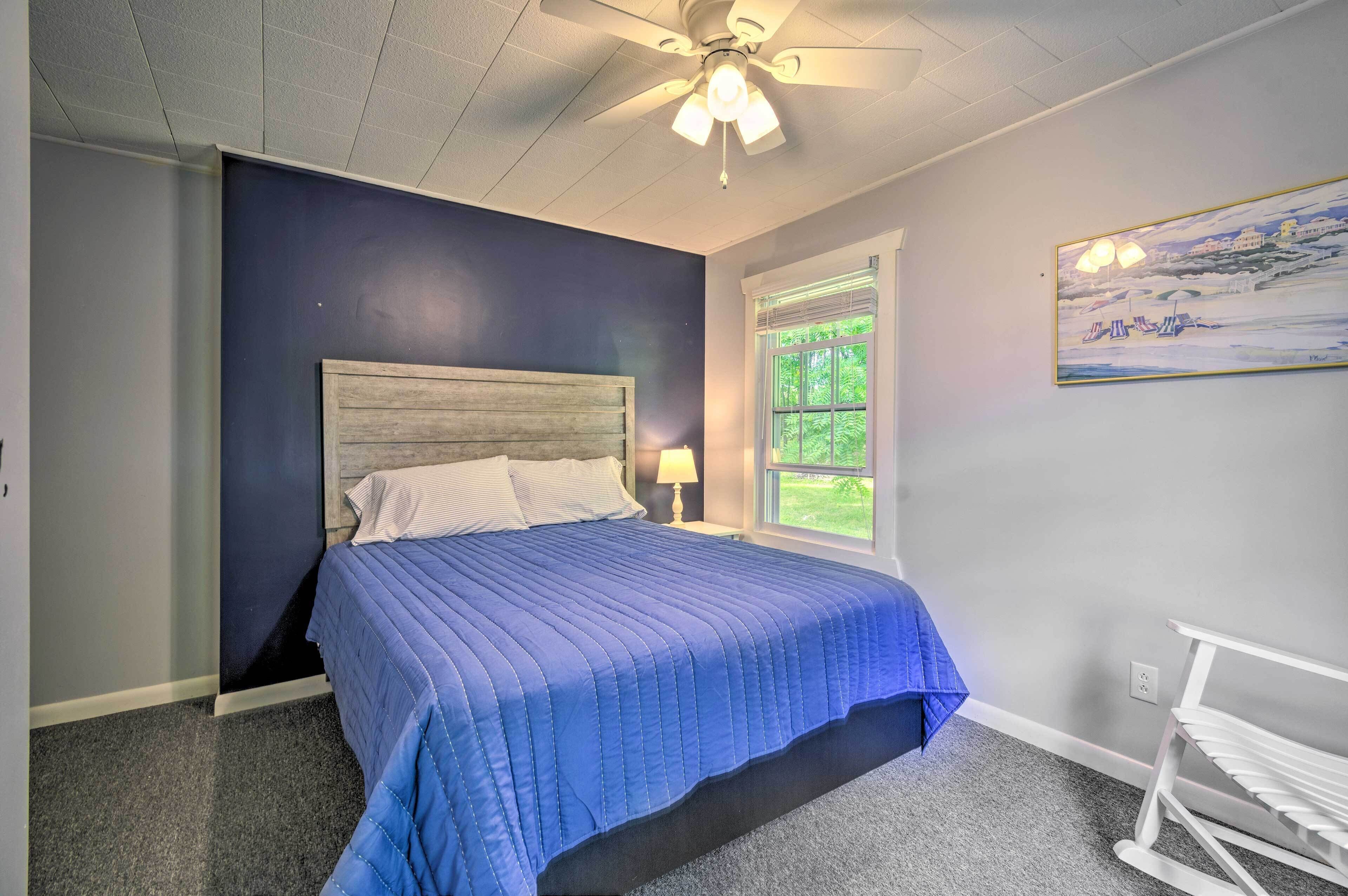 Une chambre à coucher avec un lit, un ventilateur de plafond, une fenêtre et un tableau accroché au mur.